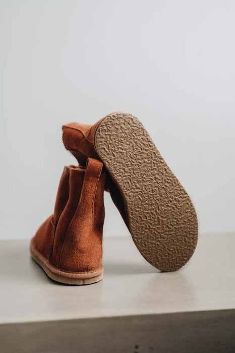 Rust coloured sheepskin slipper boot with rubber sole showing on a light grey background