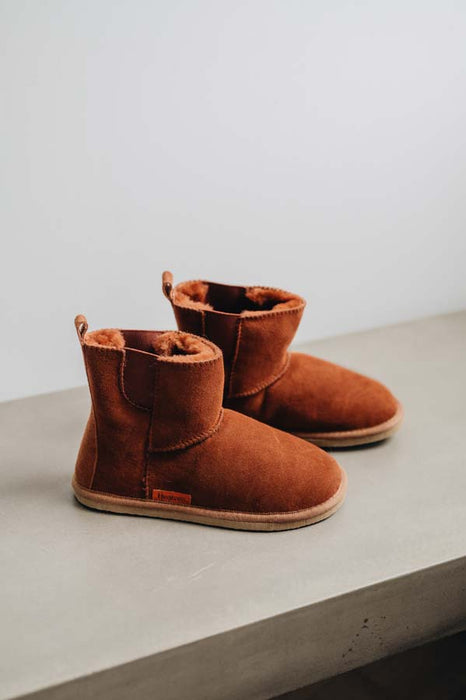 Pair of rust coloured sheepskin slipper boots on a light grey surface with a white background