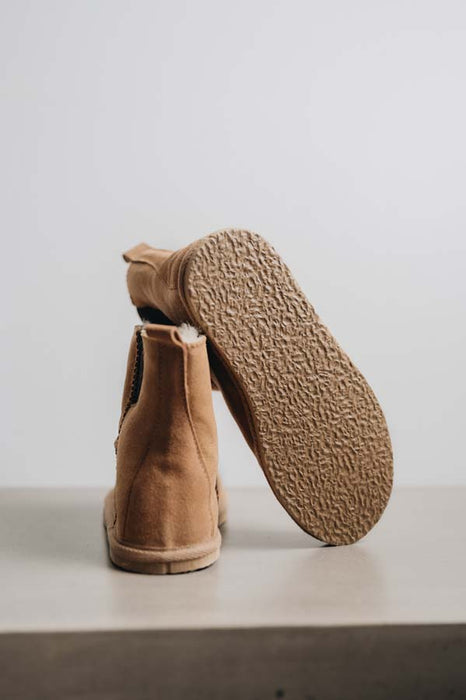 Tan sheepskin ankle boot slipper with textured rubber sole on a light grey stone background