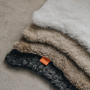 Stack of sheepskin rugs in various colours on a neutral carpet