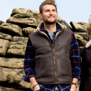 Men's Sheepskin Gilet, with collar, frotn zip and pockets. Male model stands near rocky backdrop.