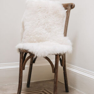 Short Wool Icelandic Sheepskin Rug in white, hung over a wooden chair