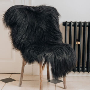A deep black/brown Icelandic Sheepskin Long Wool Rug. Draped over a brown wooden chair.