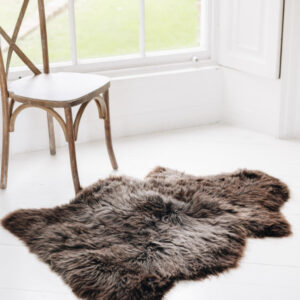 Soft Natural Brown British Sheepskin Rug contrasting against a hard and stark white wooden floor next to a traditional wooden chair in a window.