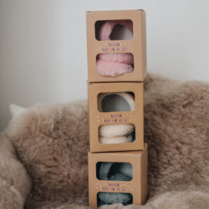 three stacked boxes of children's sheepskin earmuffs in pink, grey and tan