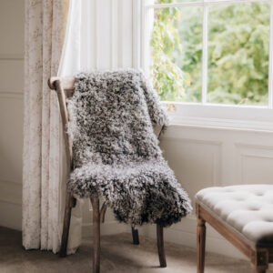 Gotland curly natural grey rug draped over a woodenchair