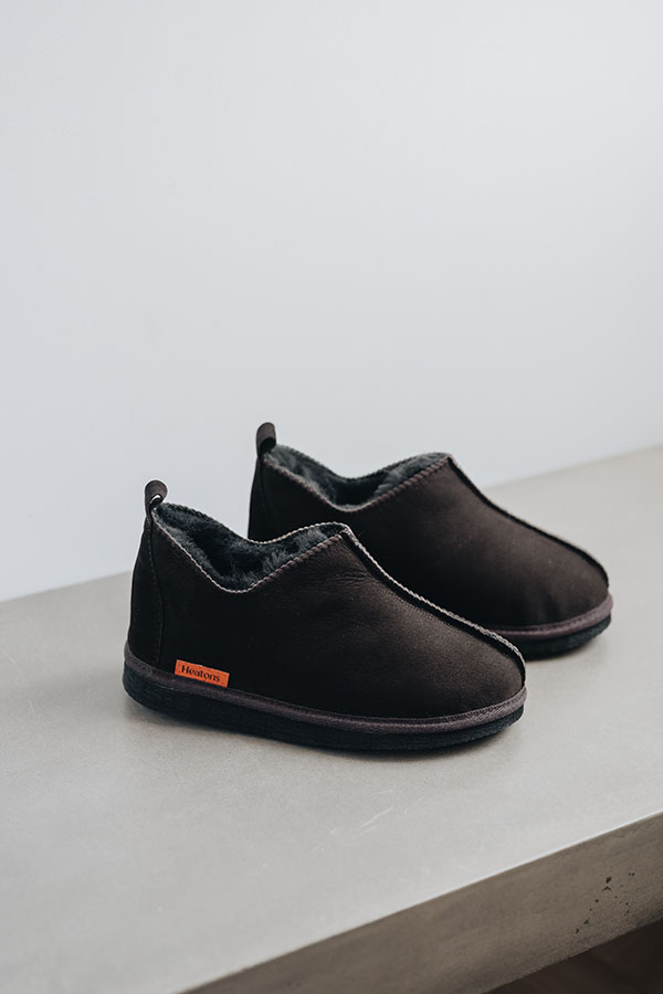 Henry men’s sheepskin slippers in brown styled on grey concrete surface