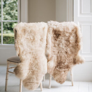 Two Natural melange coloured Swedish Sheepskin Rugs draped over the back of two wooden chairs sitting in a window