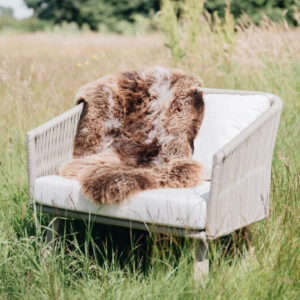 Dark Toned Rare Breed British Sheepskin Rug draped across a Garden chair in an English Meadow.